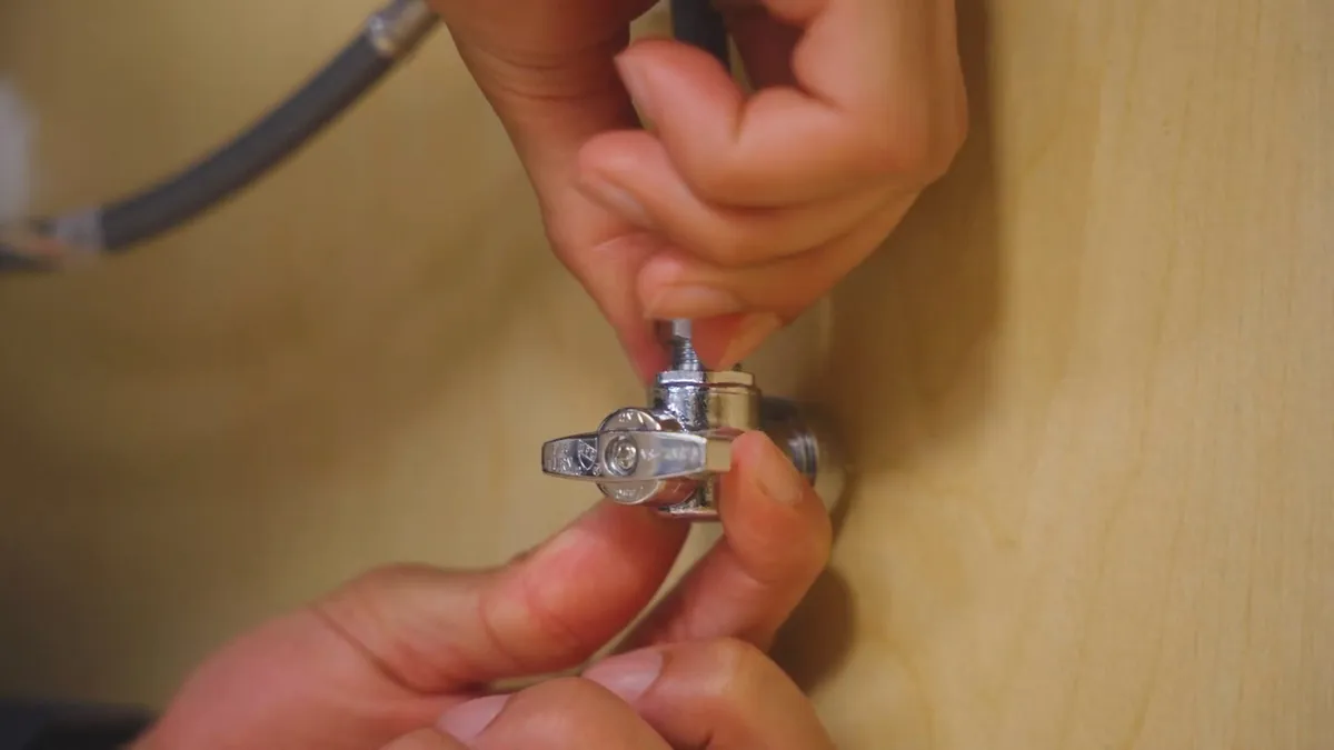 Small shutoff valve being adjusted by hand beneath a fixture during plumbing service in Bell West Ranch, Surprise, AZ