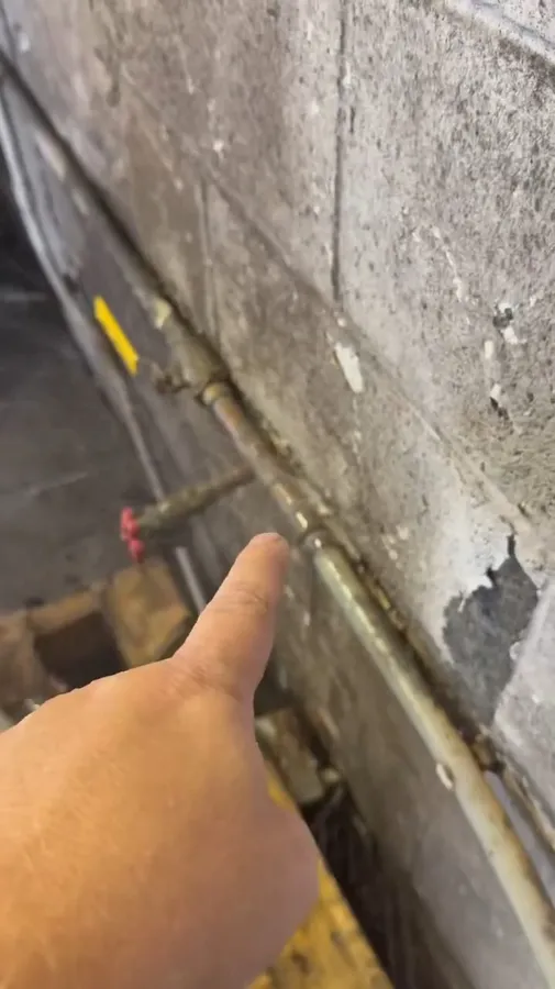 Hand pointing to a copper and plastic pipe transition fitting against a wall illustrating pool leak detection: sun city grand vs marley park az